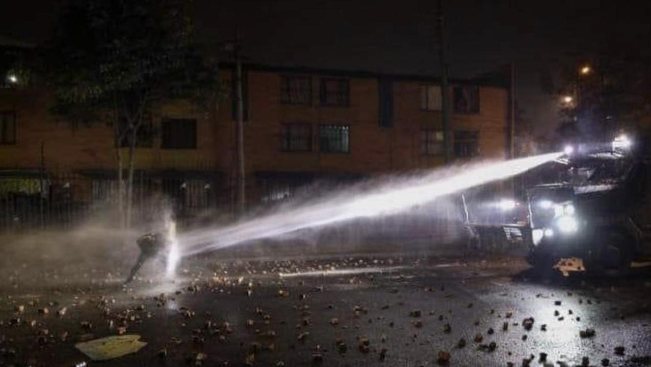 A Guy Holding The Line With A Home-Made Shield Against An Armored Water Cannon Truck During The Current Riots In Colombia